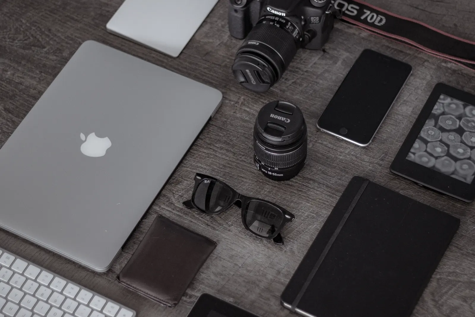 A laptop, camera, phone, and other devices arranged on a desk.