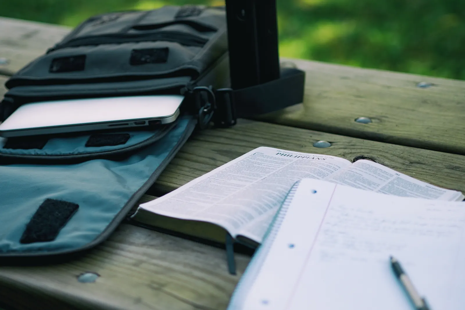 An open notebook and backpack beside a tablet outdoors.