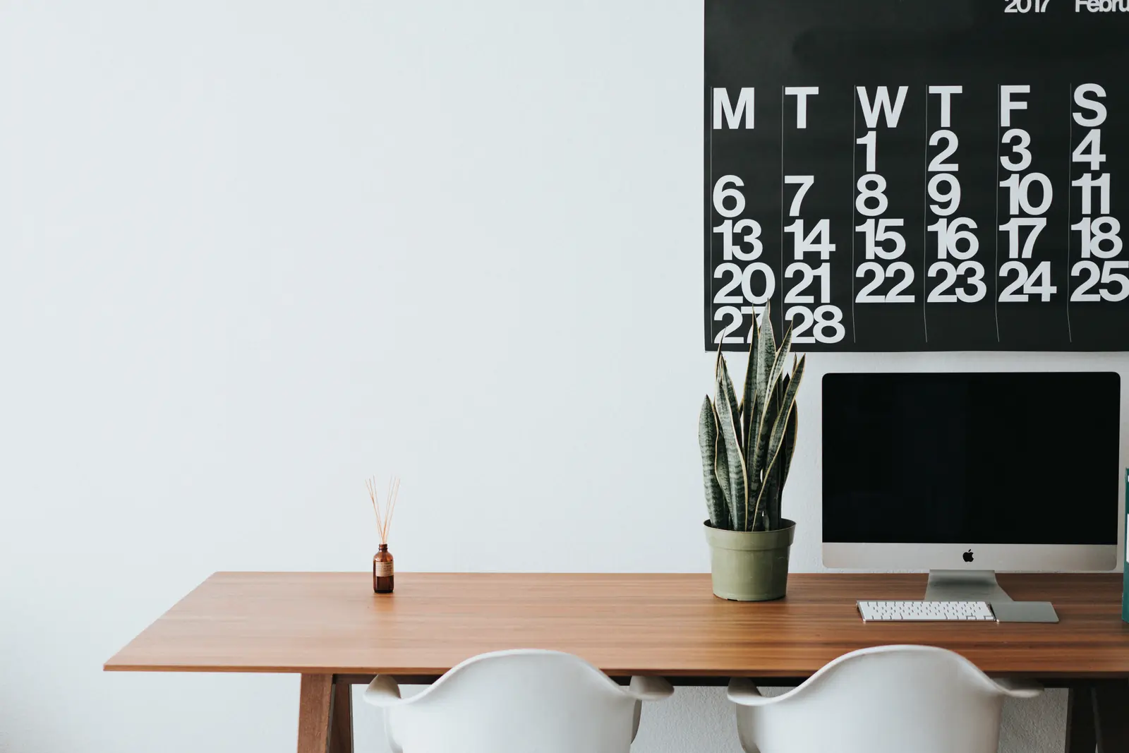 A minimalist office with a desk, computer, and wall calendar.